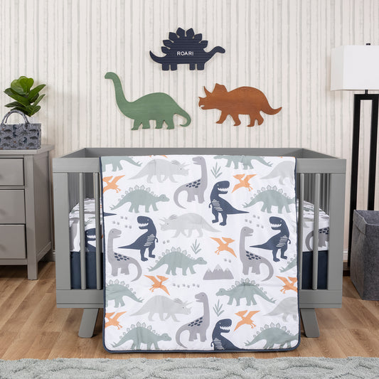 Prehistoric Dino’s 3 Piece Crib Bedding Set in stylized bedroom. The nursery quilt, fitted crib sheet, and skirt sit on a gray crib on the middle of hte room. A gray dresser, plant and storage caddy sit on the left side, and a tall standing lamp with a felt hamper sit on the right. Dino wooden decor sits hangs on the back wall with a gray rug on the floor and a natural wooden floor.