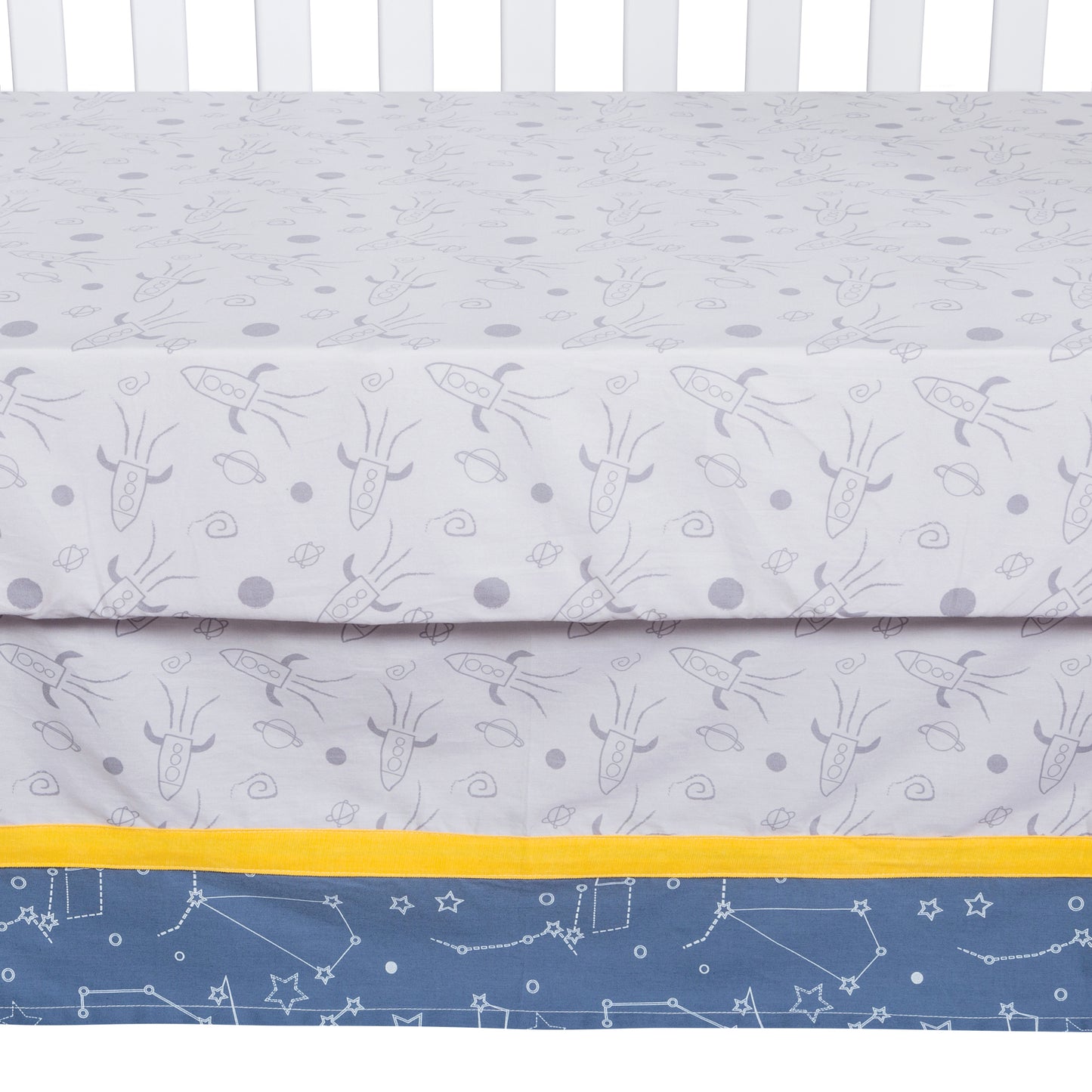 Flat panel crib skirt with 13 inch drop features a rocket ships scatter print body, star constellations trim in navy blue, gray and white with a solid yellow accent.