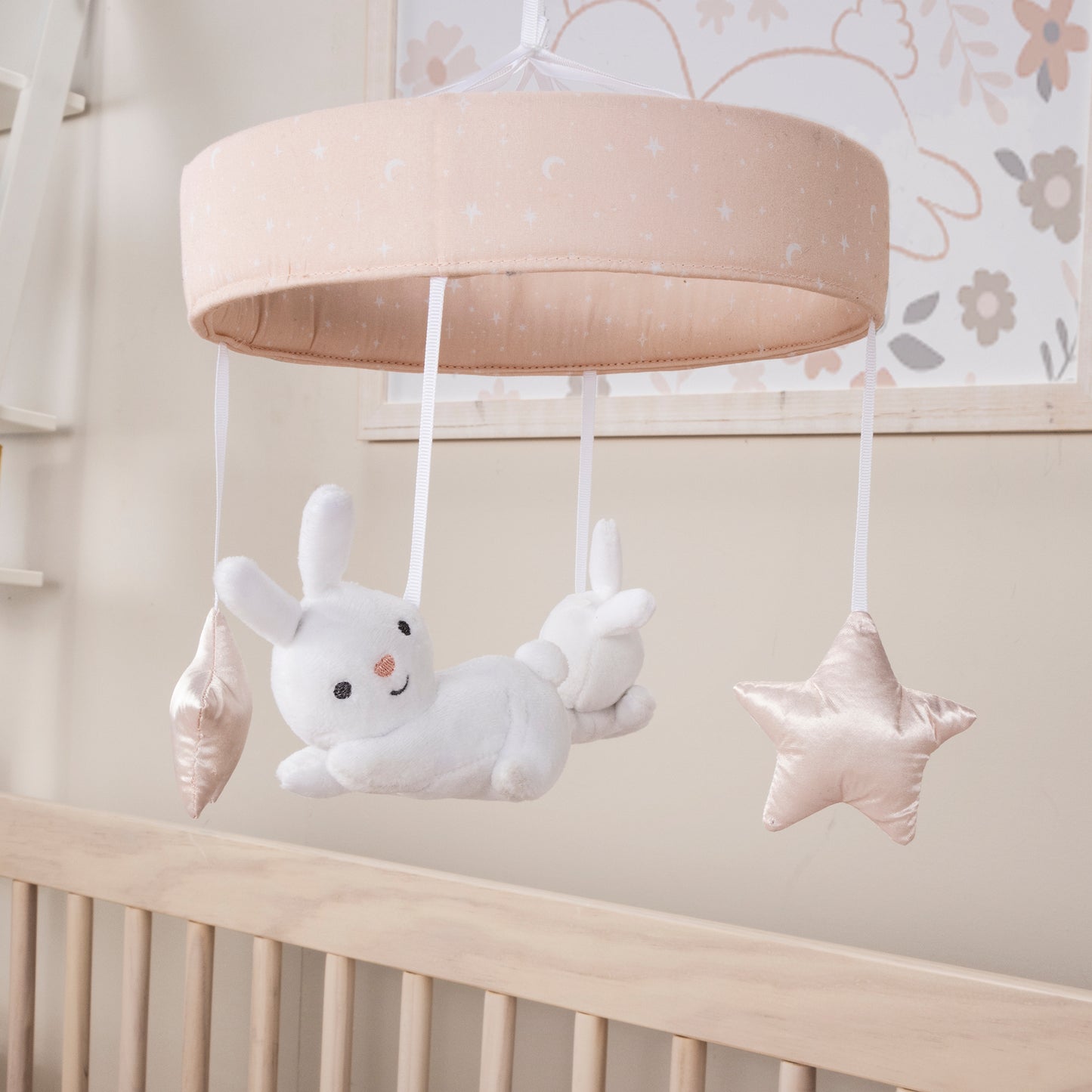 Cottontail Cloud Musical Crib Baby Mobile in stylized room; A pink and white moon and stars print on the banded mobile ring features two happy bunnies and two pink plush stars suspended from decorative white ribbons that slowly rotate to Brahms’ Lullaby. 
