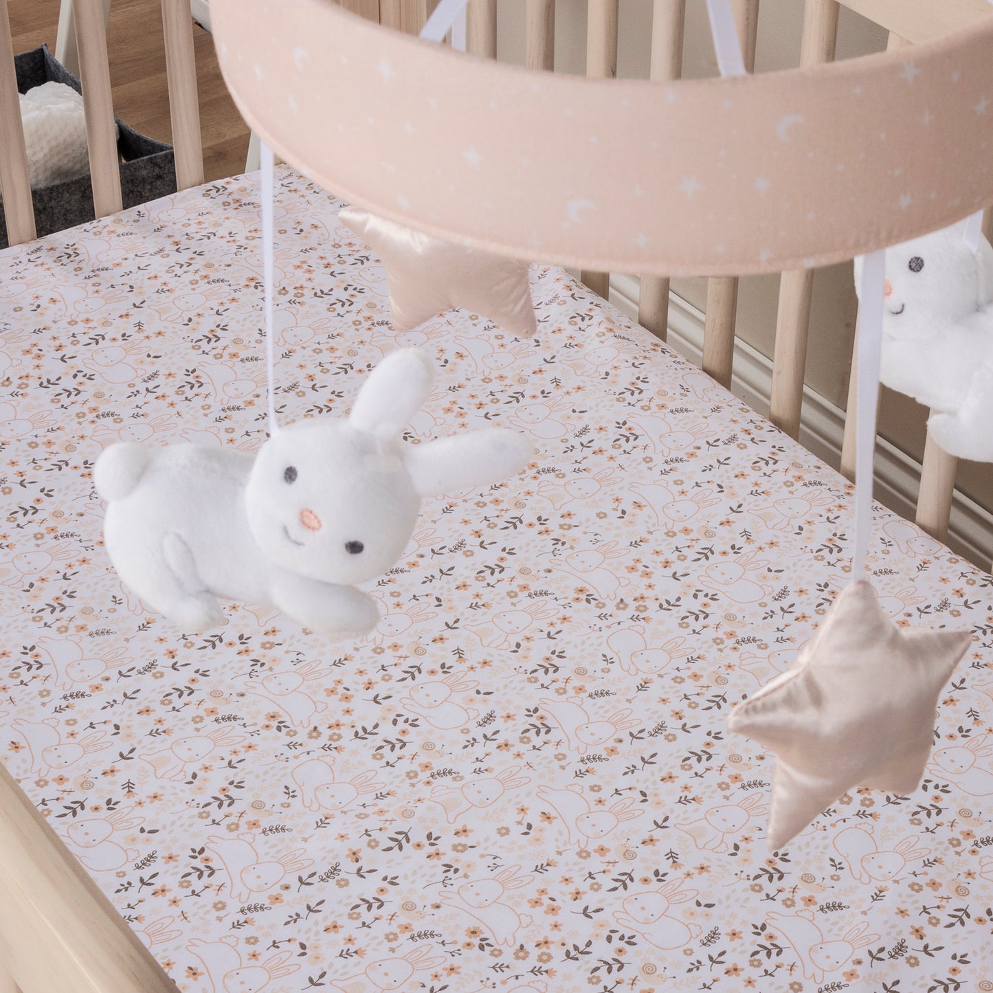 Cottontail Cloud Musical Crib Baby Mobile in stylized room; A pink and white moon and stars print on the banded mobile ring features two happy bunnies and two pink plush stars suspended from decorative white ribbons that slowly rotate to Brahms’ Lullaby. 