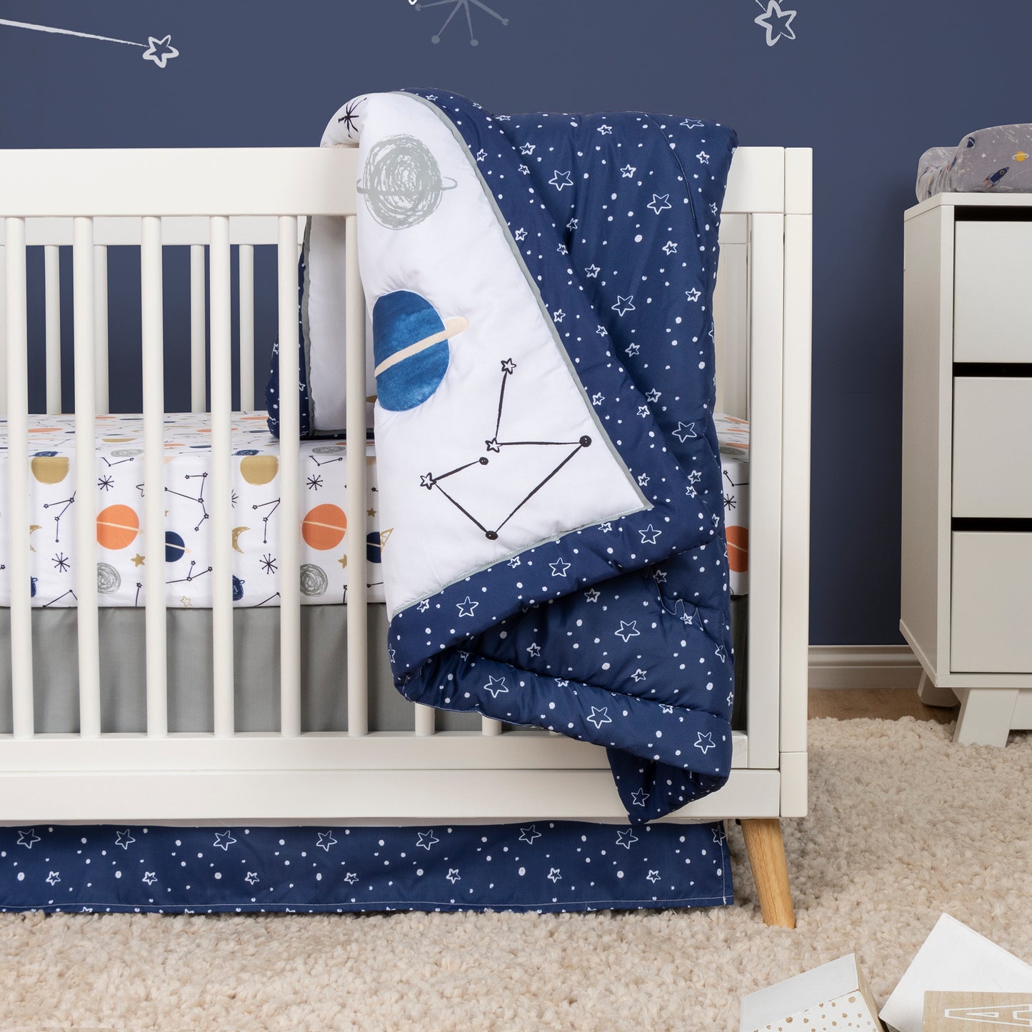 Cosmic Rocket 4 Piece Crib Bedding - stylized in room image on crib with rocket plush toy, crib quilt, crib sheet and crib skirt. All included in this space coordinating set