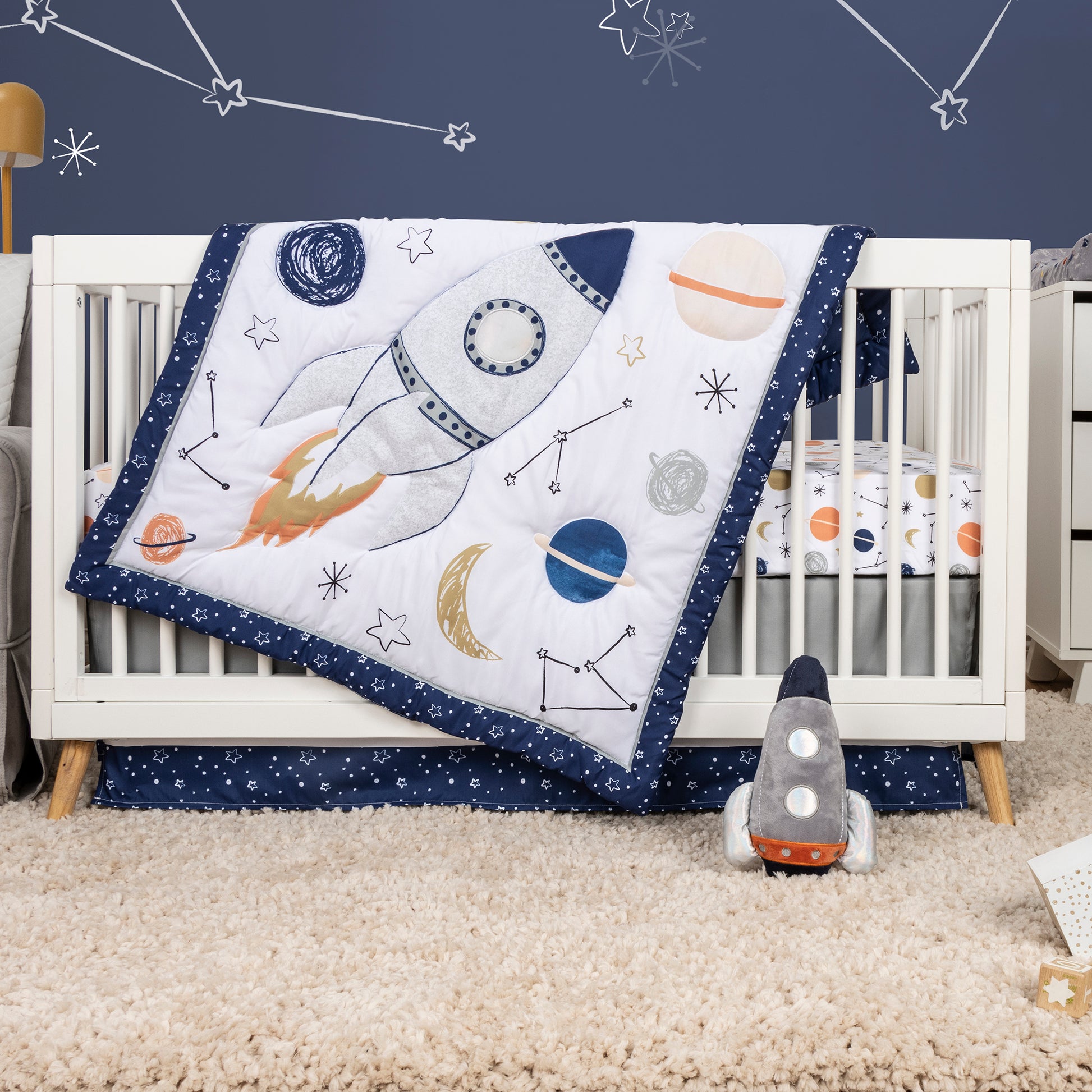  Cosmic Rocket 4 Piece Crib Bedding - stylized in room image on crib with rocket plush toy, crib quilt, crib sheet and crib skirt. All included in this space coordinating set