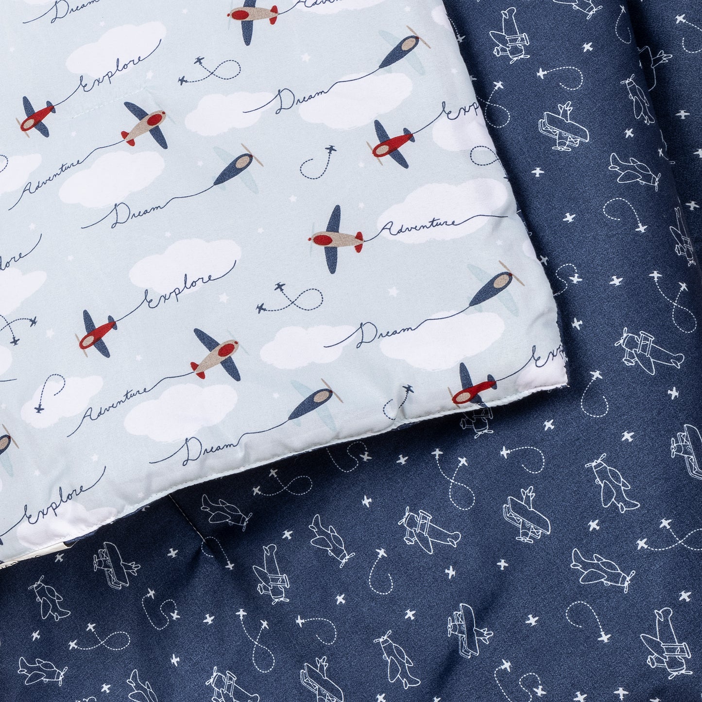 Air Travel 3 Piece Crib Bedding Set by Sammy & Lou®- stylized image of crib quilt features navy and red airplanes with clouds and a blue background. Reverse side of quilt features a navy background with celestial stars