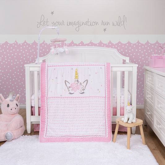 Sweet Mystical Dreams 4 Piece Crib Bedding Set sits on a white modern crib. The soft unicorn plush sits outside and in front of the crib on a wooden stool with a white rug and natural wooden flooring below it. A pink Toddler Unicorn Plush Character Chair sits to the left of the crib. A white modern dresser sits to the right of the crib with a pink storage diaper caddy with diapers in it. a Pink unicorn musical crib mobile sits above the crib and a sweet pink polka dot wallpaper captures the room.